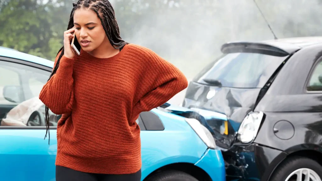 Person on the phone standing near a car accident with a blue car