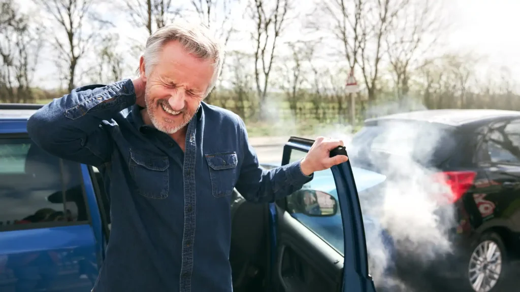 Man clutching neck beside damaged car