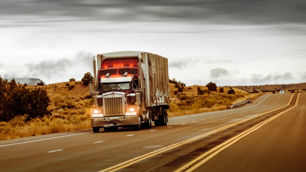 Semi-truck driving on a highway through a rural landscape.